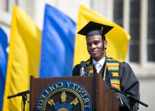A trinity college grad standing at the graduation podium ready to speak